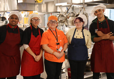 Yandel Leon Valdez, Delee Ford, Angelica Diaz and Max Rivera posing in the culinary classroom with Lisa Valentine