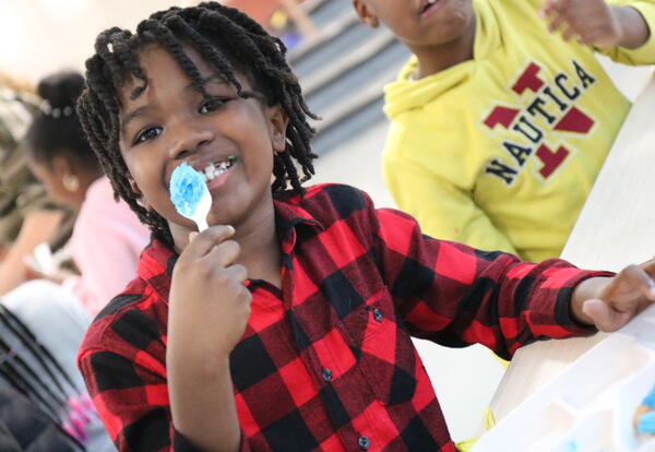 A student licks icing from a spoon while deocorating cookies.