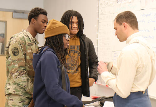 Students observing a replica of a Civil War era nightlight held by teacher Patrick Young