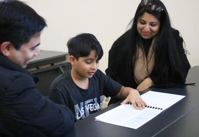 A student shares his writing journal with his parents.