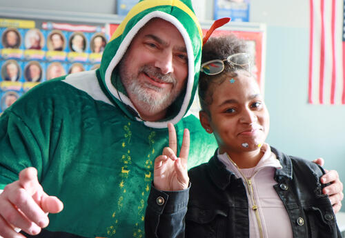 Principal Chris Martel dressed as an elf with smiling with a student