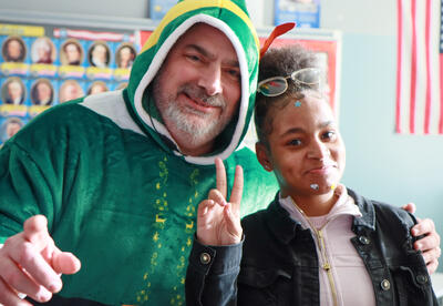 Principal Chris Martel dressed as an elf with smiling with a student