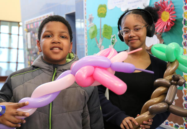 Two students display balloon animals at a school event.