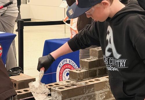 A student practices bricklaying with cement.