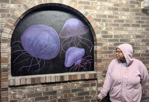Olivia Ware in front of her mural, which has purple jellyfish on a black background