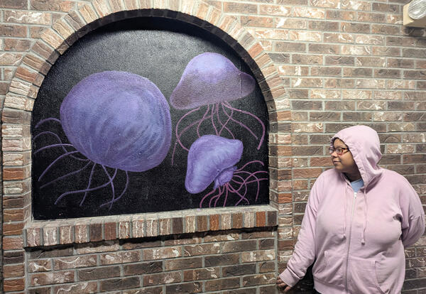 Olivia Ware in front of her mural, which has purple jellyfish on a black background