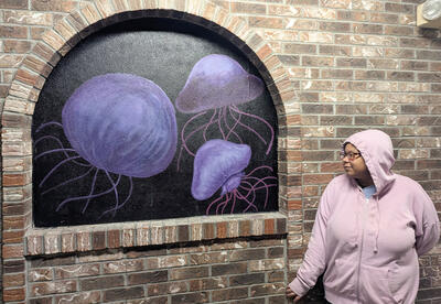 Olivia Ware in front of her mural, which has purple jellyfish on a black background