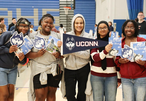 Group of five students at college fair holding brochures