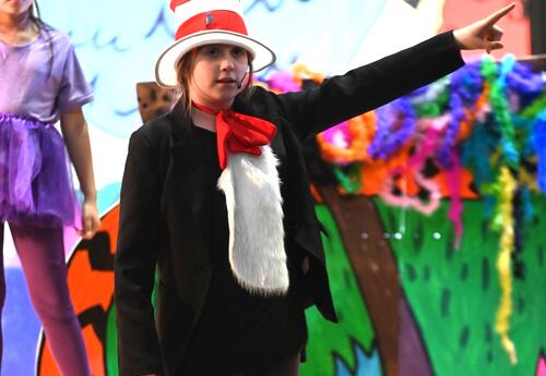 A student is dressed up like Cat in the Hat and singing on a stage.