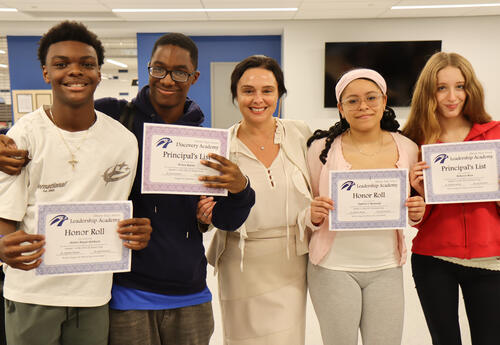 Four students holding their honor roll certificates with Principal Commerford