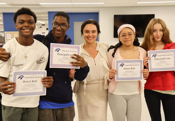 Four students holding their honor roll certificates with Principal Commerford