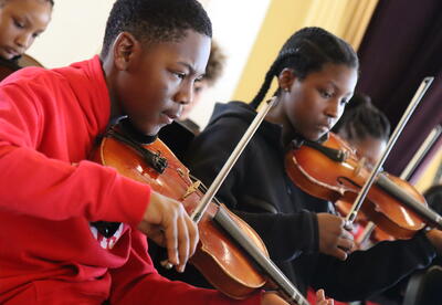 Two students in the orchestra practice the violin.