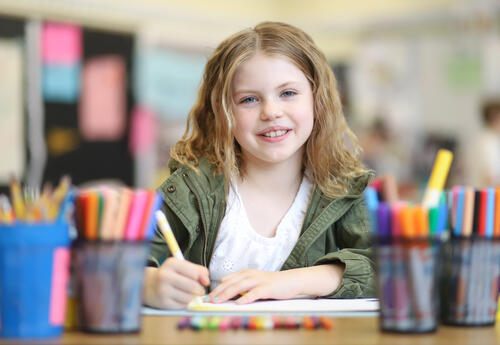 Elementary student smiling while drawing, surrounded by art supplies