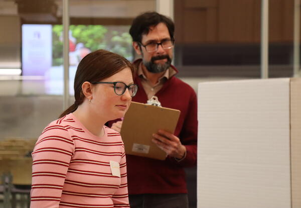 A student presents her science fair project to a judge.