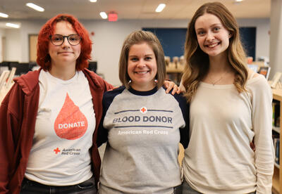Two students standing to the left and right of blood drive adviser Alicia Abdul