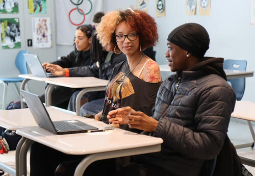 Photo of two students in classroom working on laptop