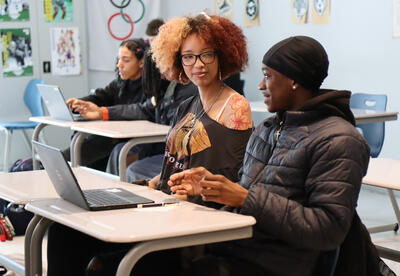 Photo of two students in classroom working on laptop