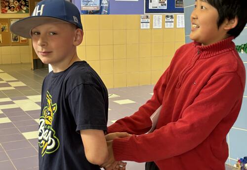 A student pretends to escort out another student in handcuffs.s.