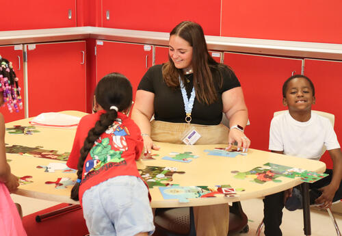 Photo of teacher working with three students at a puzzle station