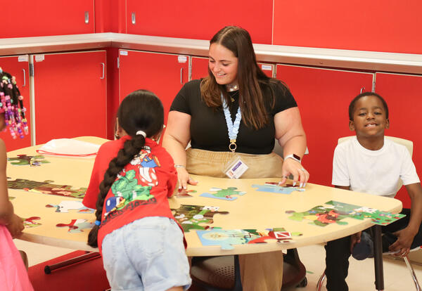 Photo of teacher working with three students at a puzzle station