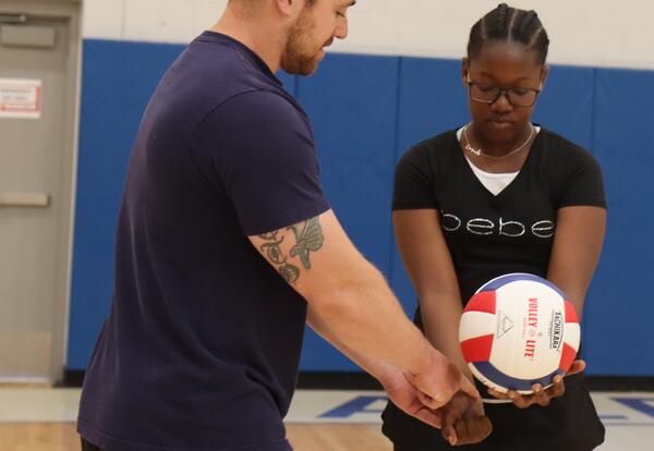 A PE teacher teaches a student how to serve a volleyball.