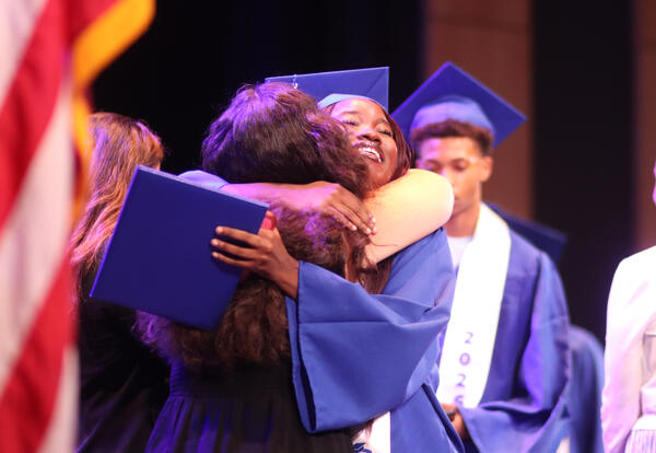 Photo of graduate hugging an administrator on stage at graduation