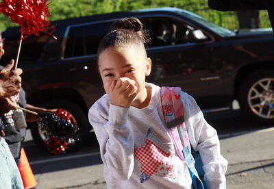 A student smiles at her teachers and school staff as she walks in during a clap in.