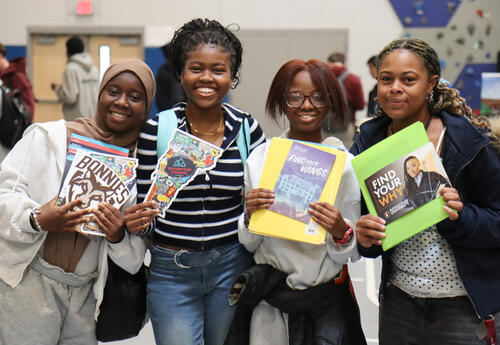 Group of four students at college fair holding brochures