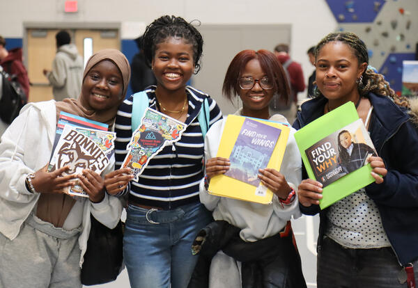 Group of four students at college fair holding brochures