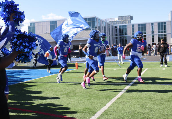 Football players running onto the field with the Falcon mascot