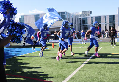 Football players running onto the field with the Falcon mascot