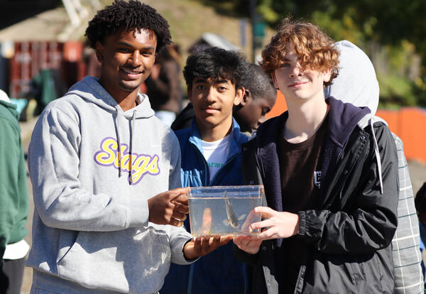 Three students holding a tank with a fish