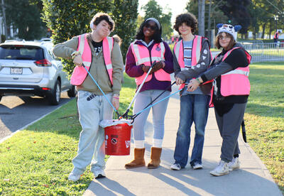 Four students posing with trash buckets and trash grabbers
