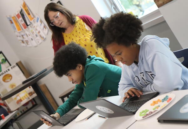 Two students complete a tech lab with help from a teacher.