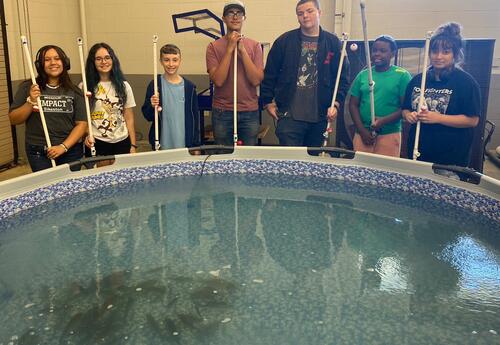 Students pose in front of swimming pool with fishing rods