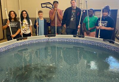 Students pose in front of swimming pool with fishing rods