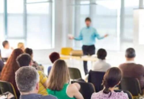 A blur image of a man standing in front of people sitting at a meeting