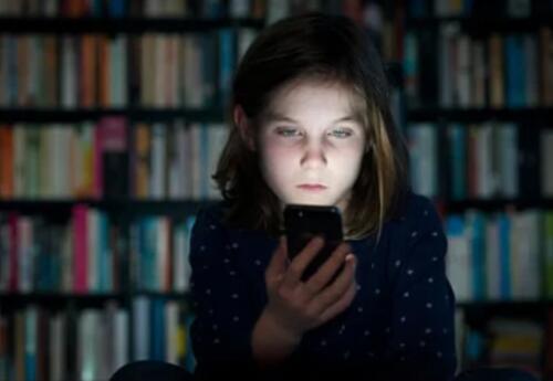 a young girl in a dark library looking at her cell phone