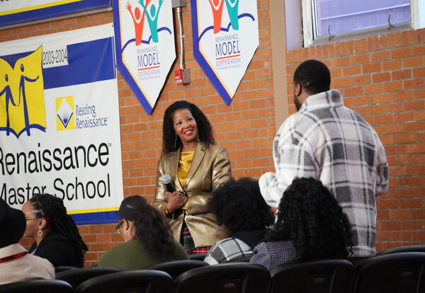 A woman speaker looking at a guest standing up answering a question in an event setting