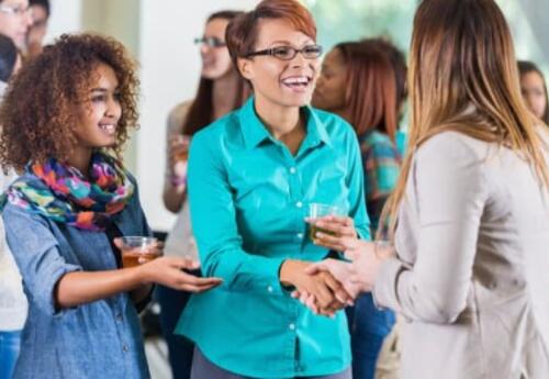 People at a meeting, mother with her daughter by her side greeting another person.