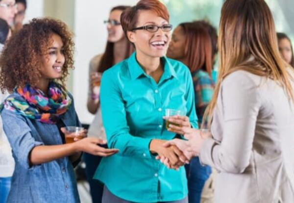 People at a meeting, mother with her daughter by her side greeting another person.
