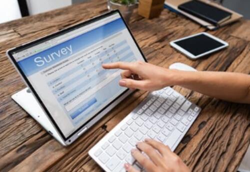 Picture of a computer on a table and someone pointing their finger at an area on the screen that reads survey.