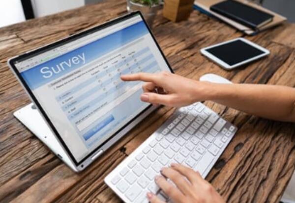 Computer on a table, a finger pointing to an area on the screen, screen reads survey.
