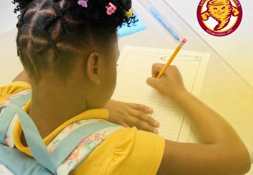 A Laurel School District elementary student completes a classroom writing activity at a desk. The district logo appears in the upper-right corner.
