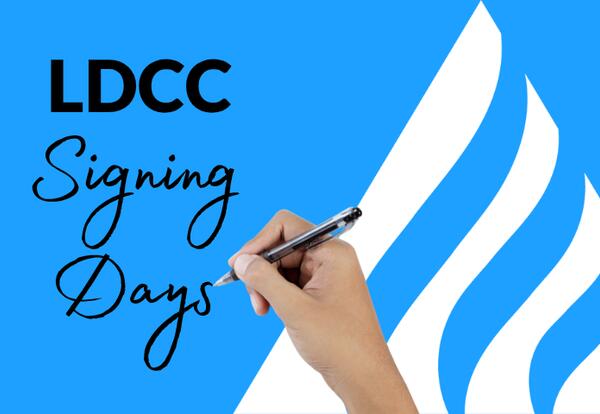 Graphic for “LDCC Signing Days” featuring a bright blue background with large black text reading “LDCC” and script-style text reading “Signing Days.” A close-up image of a hand holding a pen appears in the center, as if signing a document. White abstract 