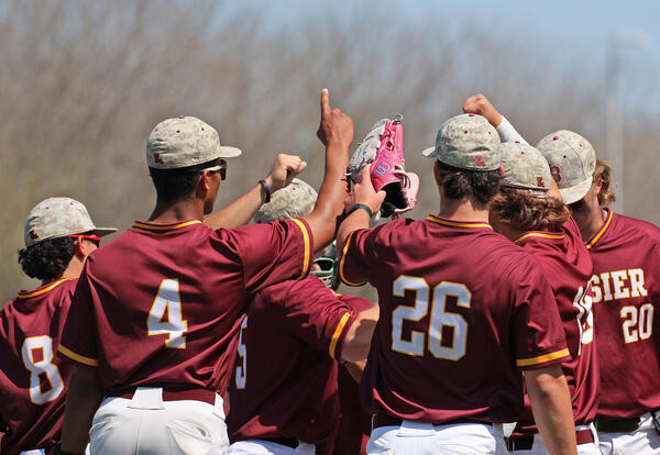 BPCC baseball team huddles with hands and glove raised.