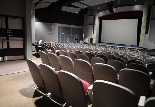 Empty auditorium with rows of seats facing a stage and large screen.