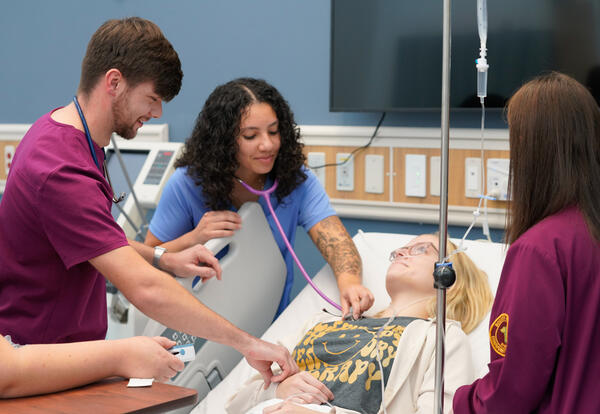 Nursing students using stethoscopes to listen to a patient's heartbeat