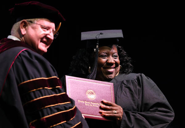 Graduation photo with student receiving diploma wearing cap and gown