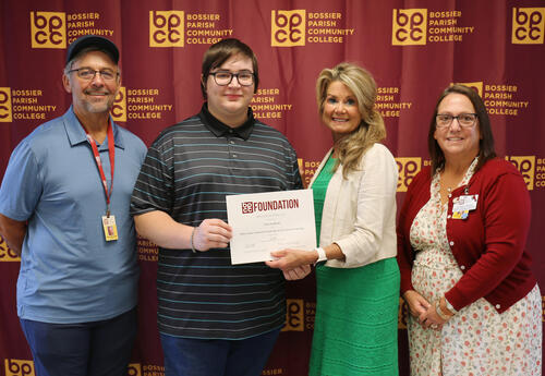 Four people standing for a group photo; the two people in the middle are holding a piece of paper for a presentation